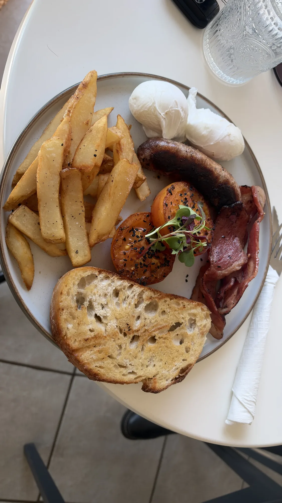 A full breakfast plate with chips, sausage, bacon, tomato and toast