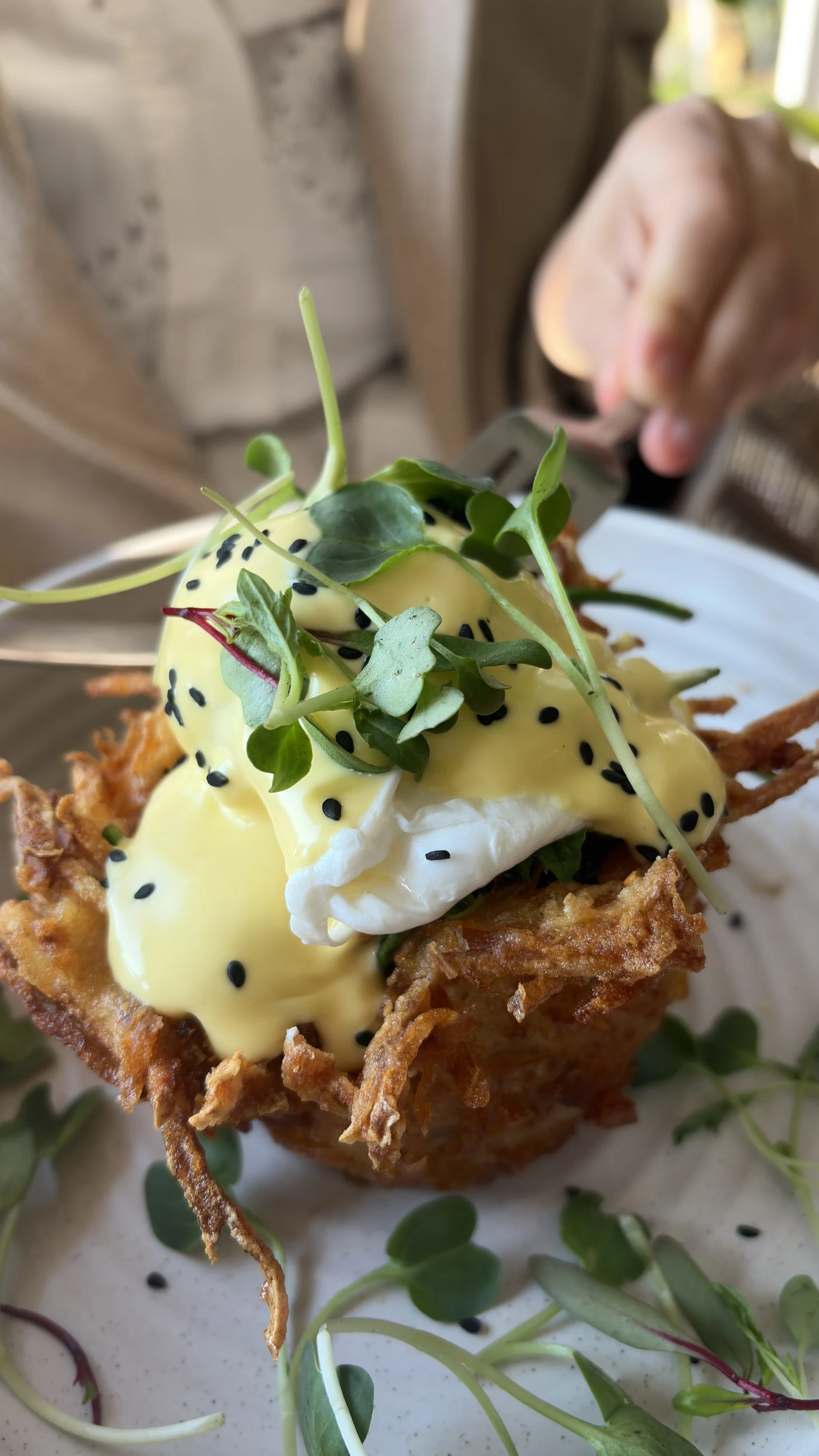 A knife cutting into a poached egg on a rosti