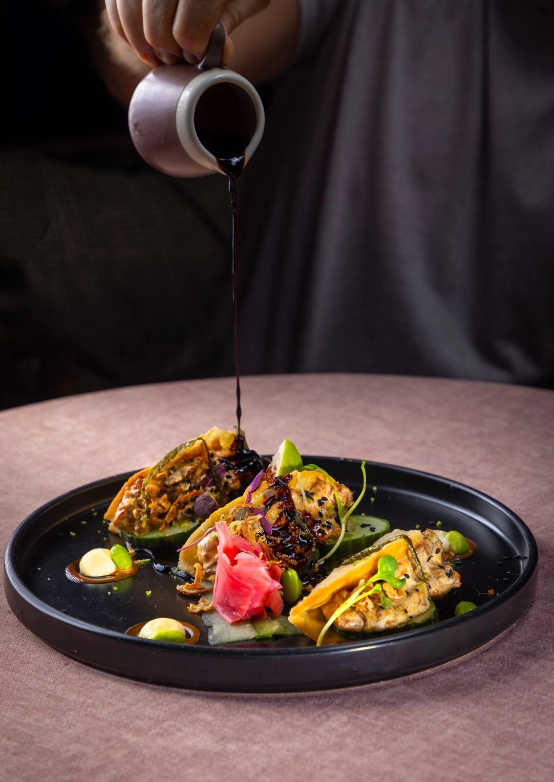 Sauce poured over crispy fried sushi tacos on a dark plate