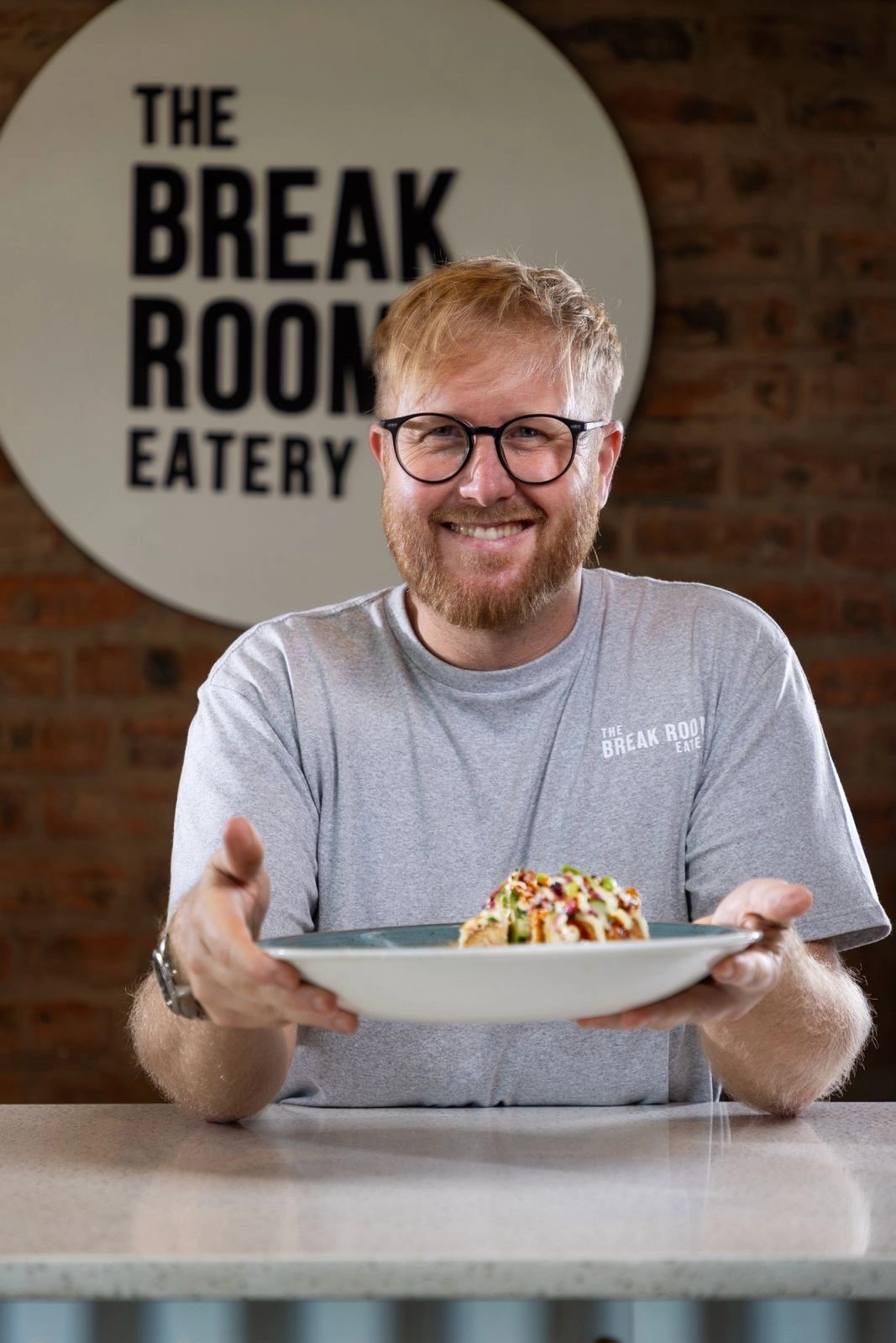 Lee Hankey smiling and holding out a plate at the counter