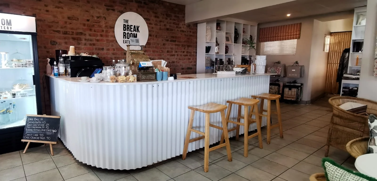 The white counter with wooden bar stools and the cake fridge