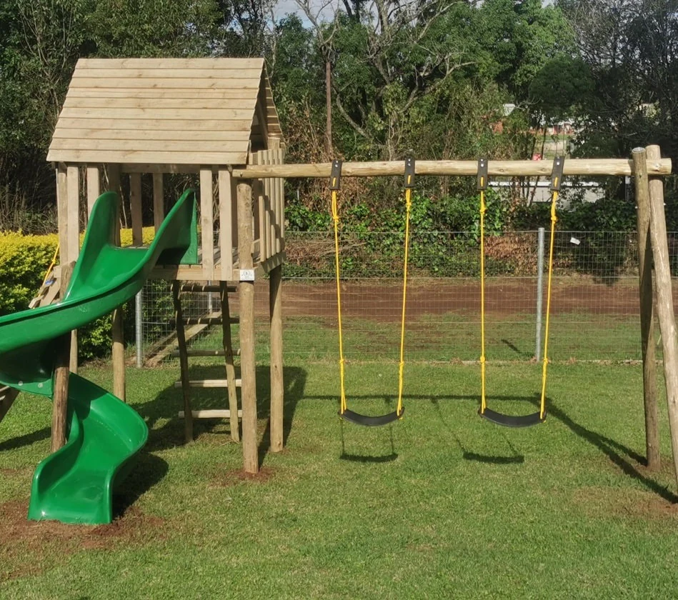 The wooden jungle gym with a slide and swings on the grass