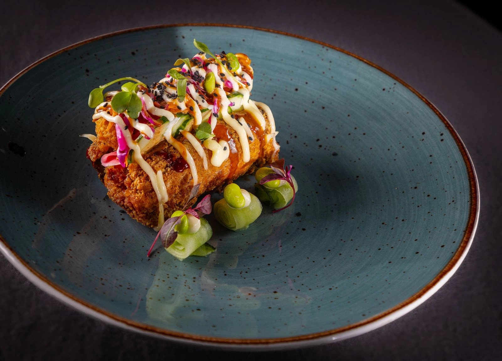 The SushiDogg on a blue plate, loaded with sauces, edamame and micro greens